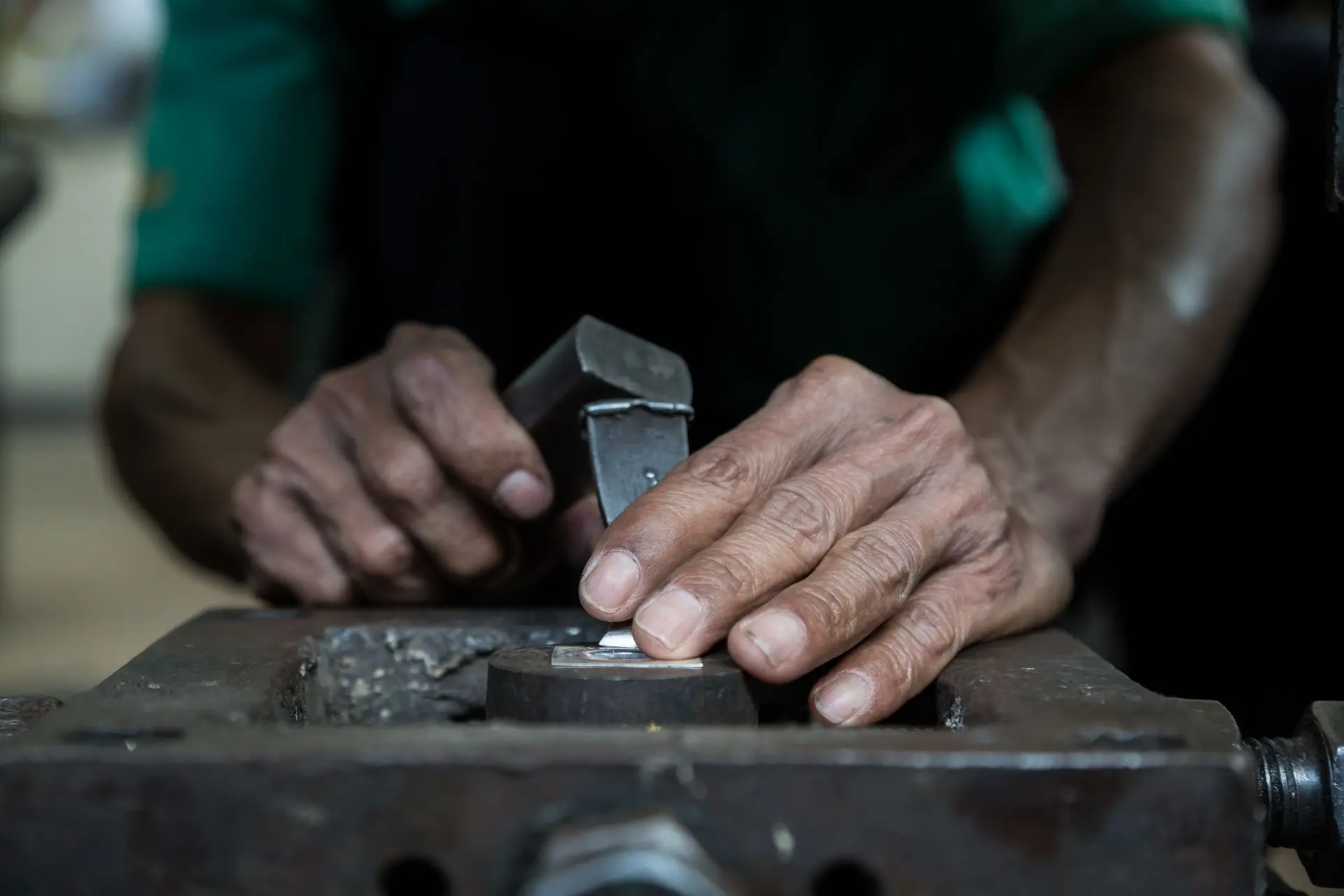 Close-up of a Thai artisan’s hands engraving a floral motif on a silver crucifix pendant, showing intricate details and textures, highlighting Thai Design’s championing of traditional silversmith techniques.
