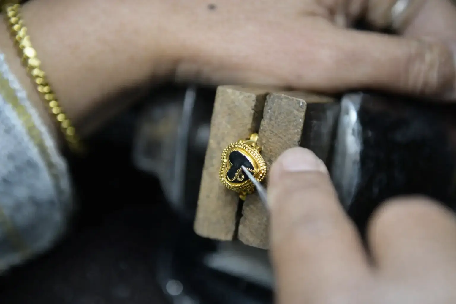 Thai goldsmith hand-engraving a yellow gold heart-shaped locket pendant with milgrain beading, evoking the heritage of Thai gold craftsmanship