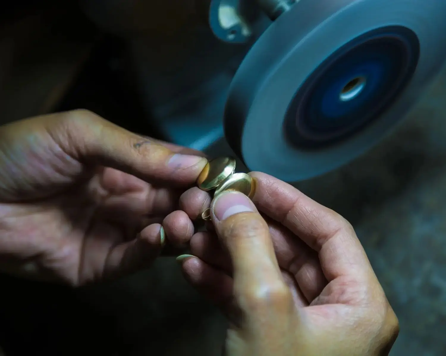 Close-up of a Thai goldsmith’s hands crafting a gold locket pendant by hand, using a filing wheel to create a polished texture